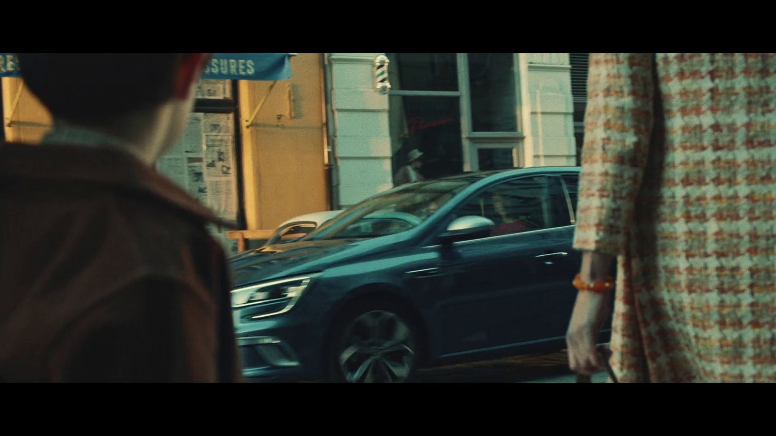 a woman walking down a street next to a blue car