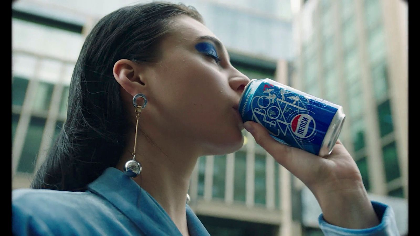 a woman drinking a can of pepsi in front of a building