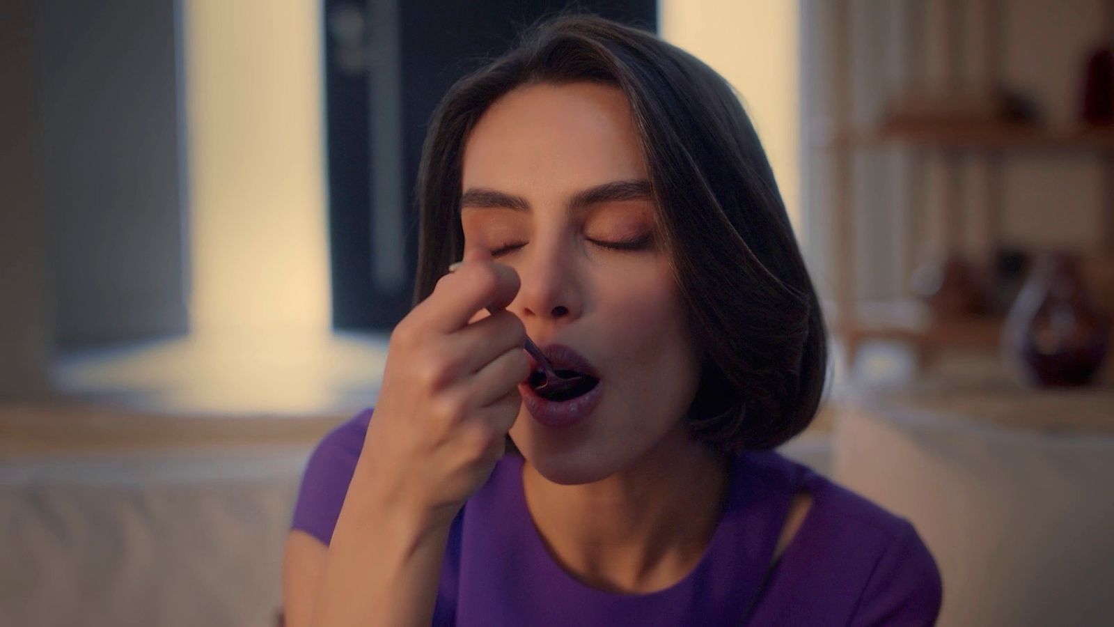 a woman in a purple shirt is putting something in her mouth