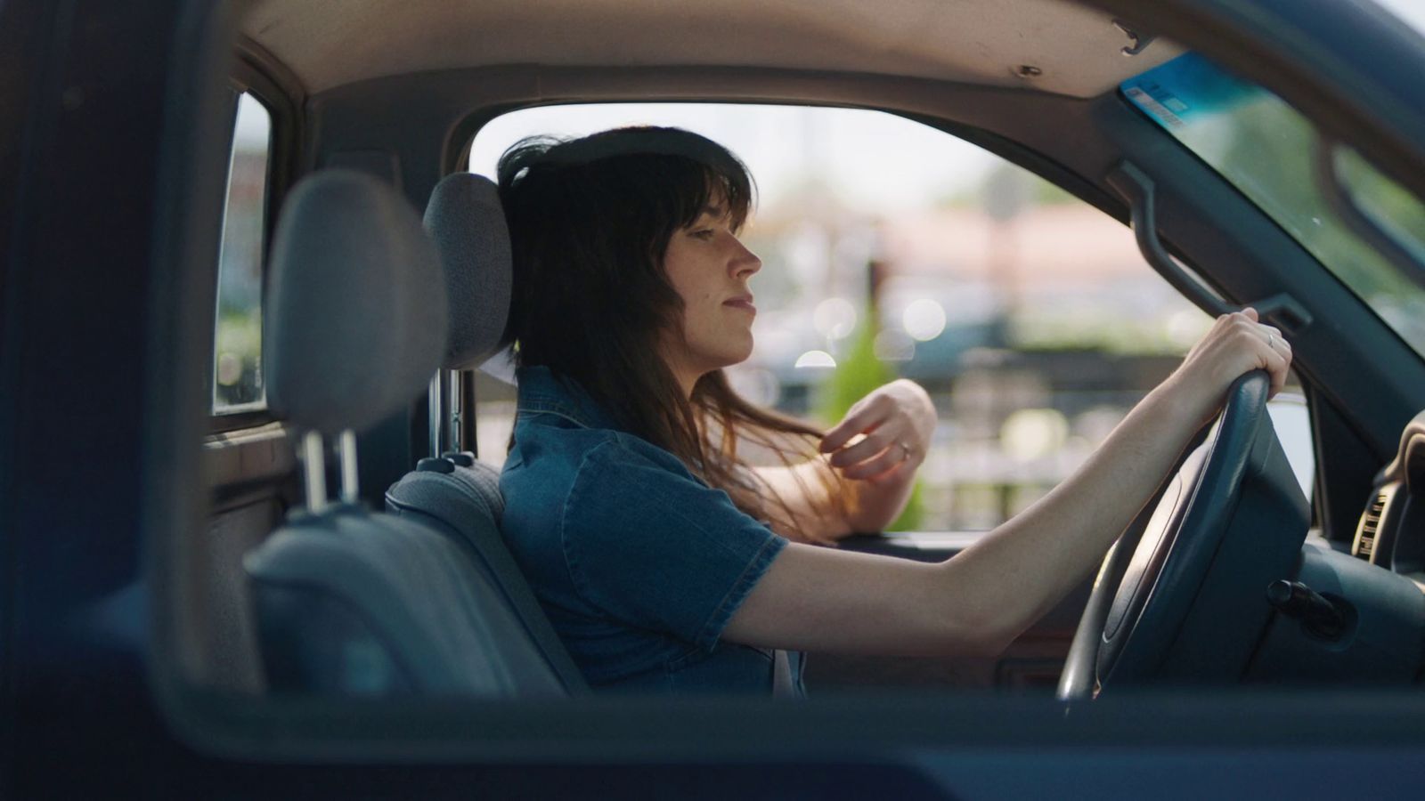 a woman sitting in a car with her hand on the steering wheel