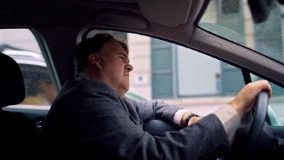 a man sitting in a car with his hand on the steering wheel