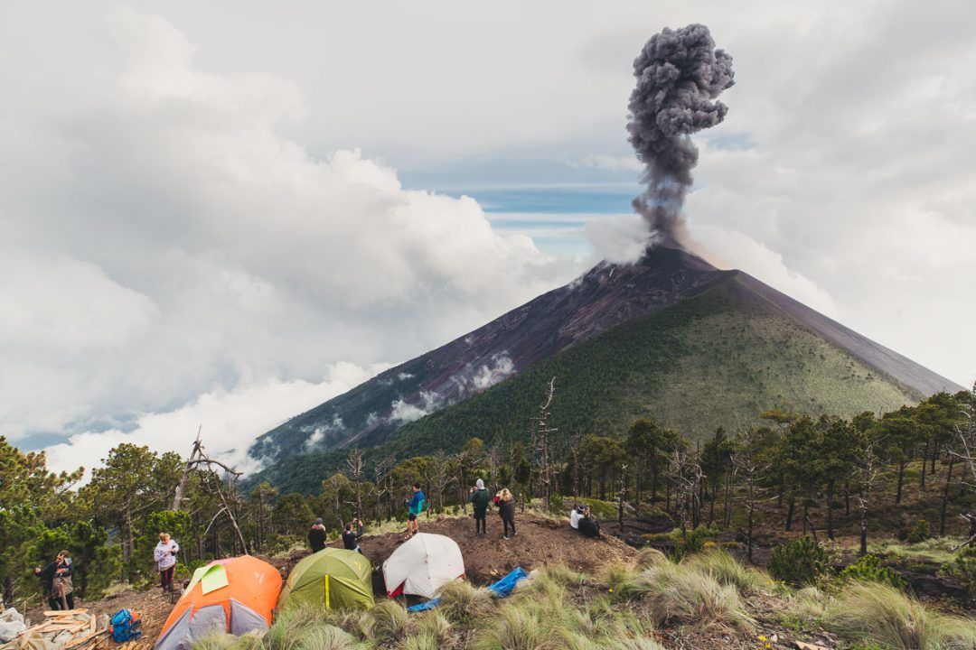 a group of people standing around tents in front of a volcano