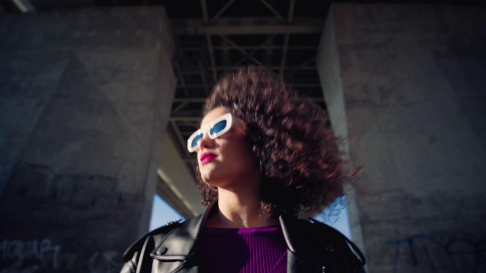 a woman wearing sunglasses standing under a bridge