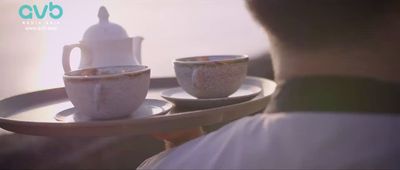 a person holding a tray with cups and saucers on it