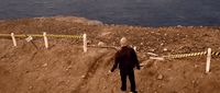 a man standing on top of a dirt hill next to a body of water