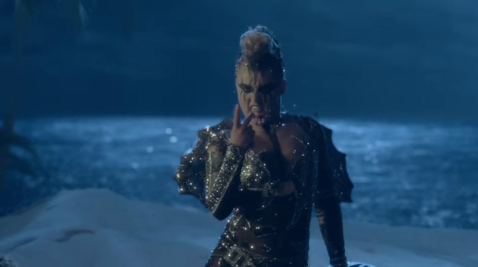 a woman in a gold outfit standing in front of a body of water