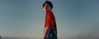 a boy in an orange shirt is standing on a beach