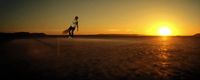 a woman walking across a field at sunset