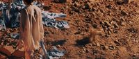 a man standing in the dirt next to a pile of clothes