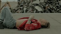 a woman laying on the ground in front of a pile of scrap metal