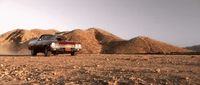 a car driving through a desert with mountains in the background