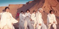 a group of men in white outfits standing in front of a mountain