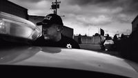 a black and white photo of a man leaning on a car