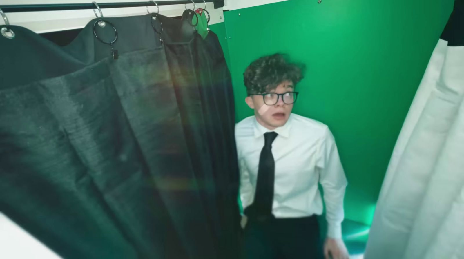 a young man wearing glasses and a tie standing in front of a curtain