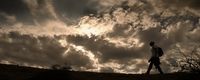 a man walking up a hill under a cloudy sky