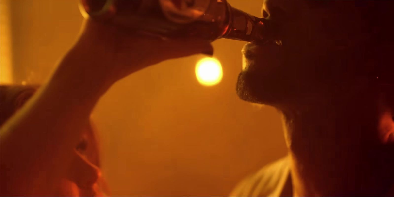 a man drinking from a beer bottle in a dimly lit room