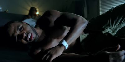 a shirtless man laying on a bed in the dark