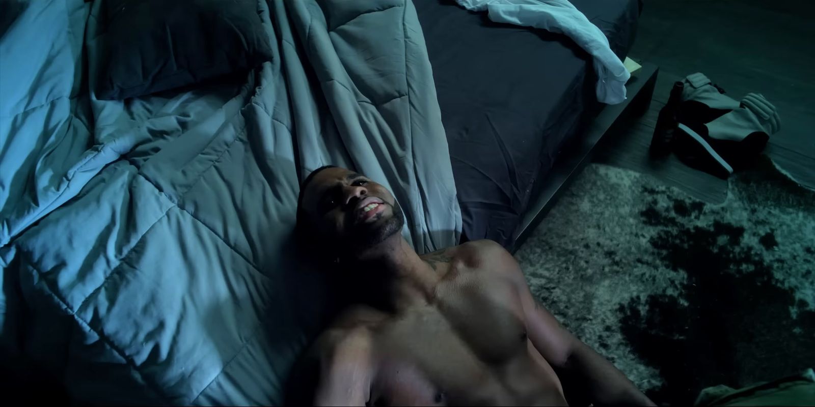 a shirtless man laying on a bed in a dark room