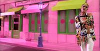 a woman is walking down the street in front of a pink building