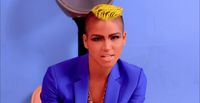 a woman with a yellow mohawk sitting in front of a blue wall