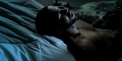 a shirtless man laying on a bed in the dark