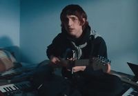 a man sitting on a bed playing a guitar