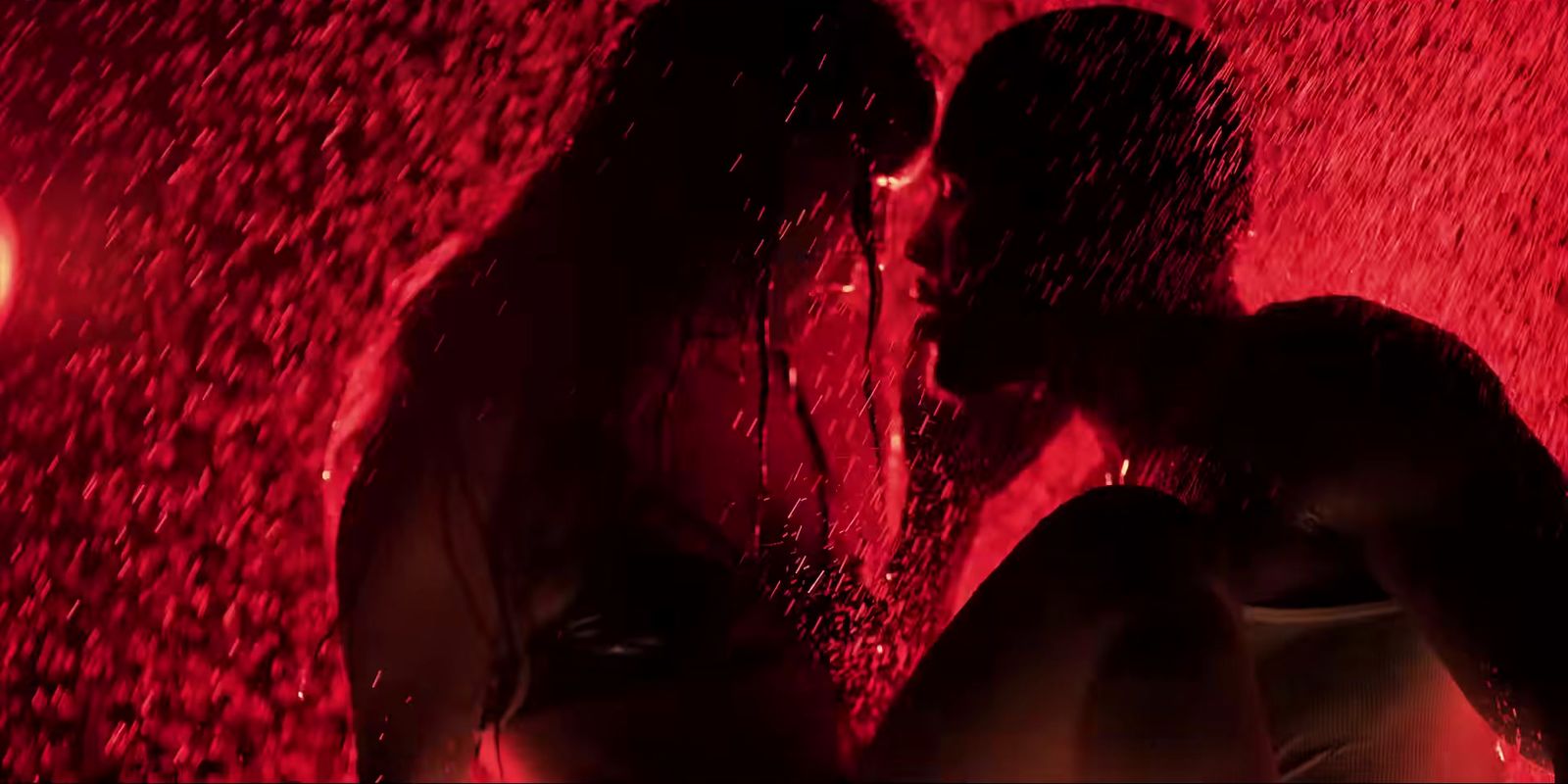 two people standing under a red light in the rain