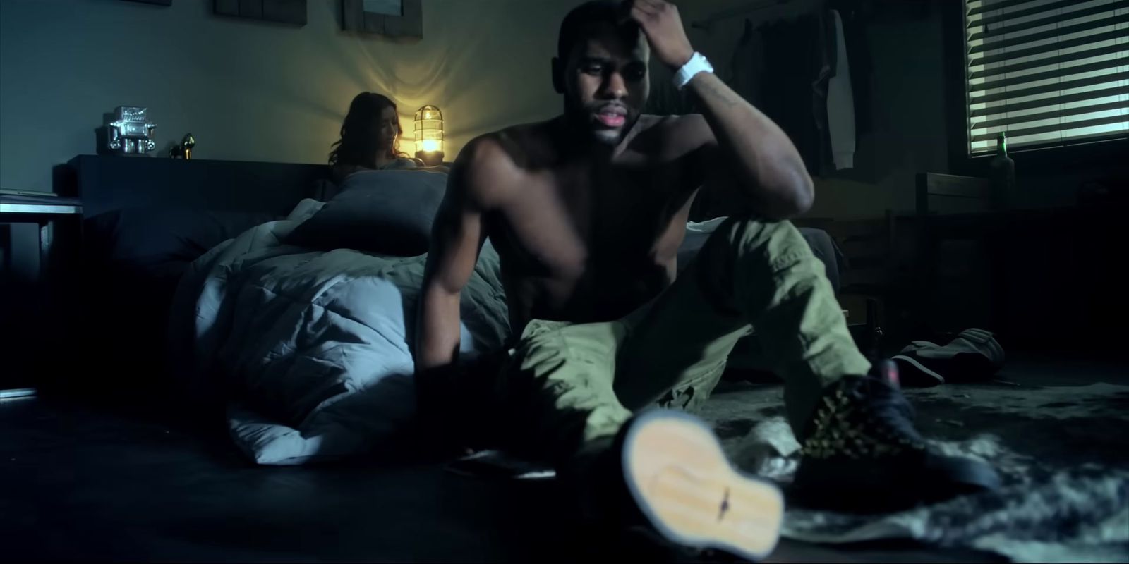 a shirtless man sitting on a bed in a dark room