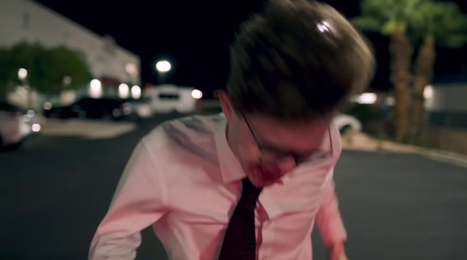 a man in a pink shirt and tie walking down a street