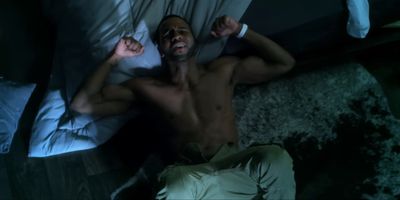 a shirtless man laying on a bed in the dark