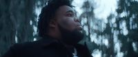 a man with dreadlocks standing in front of trees