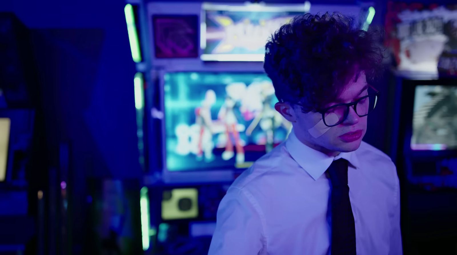 a man wearing glasses and a tie standing in front of televisions