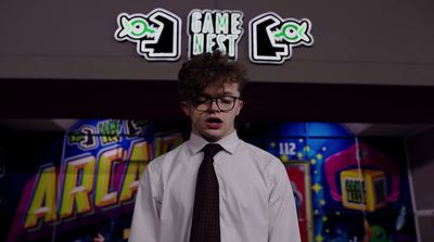 a man wearing a tie and glasses standing in front of a neon sign