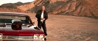 a man standing next to a red car in the desert