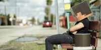 a man sitting on a bench with a paper mask on his head