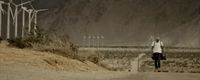 a man standing on a dirt road next to a wind farm