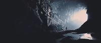 a man standing in a cave looking out at the water