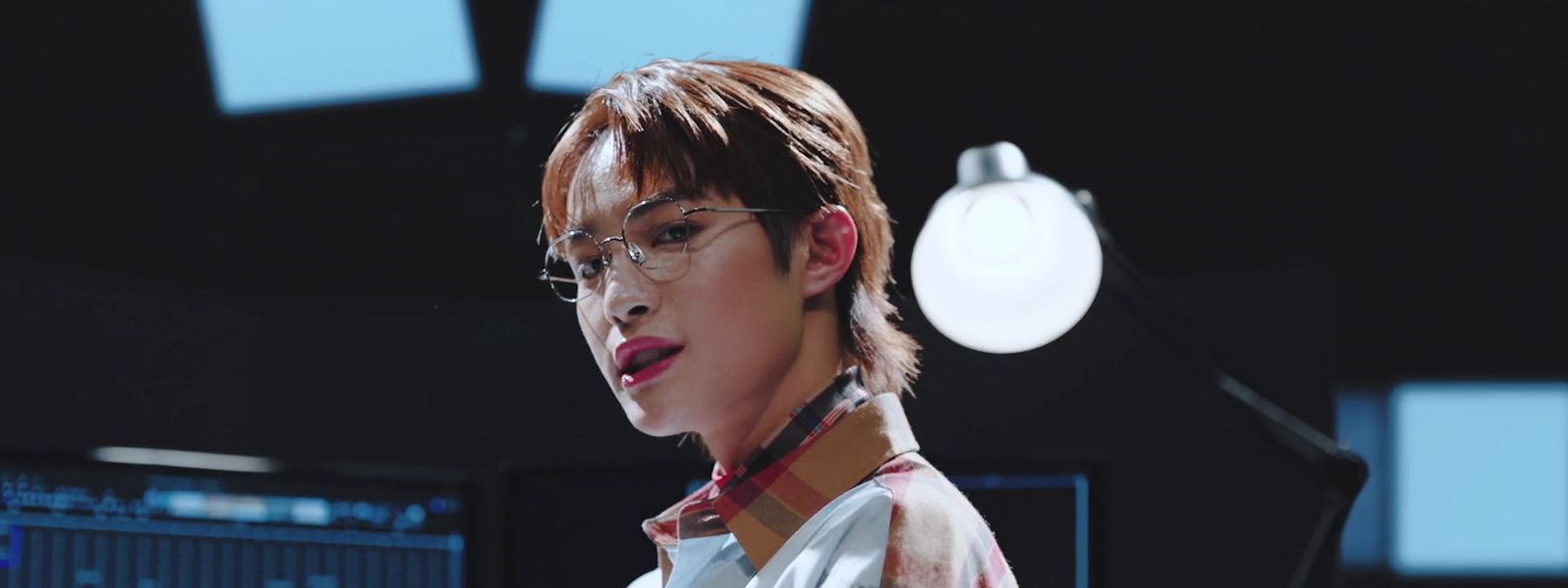 a man with glasses and a tie standing in front of a monitor