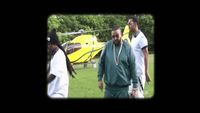 a group of people walking around a field with a helicopter in the background