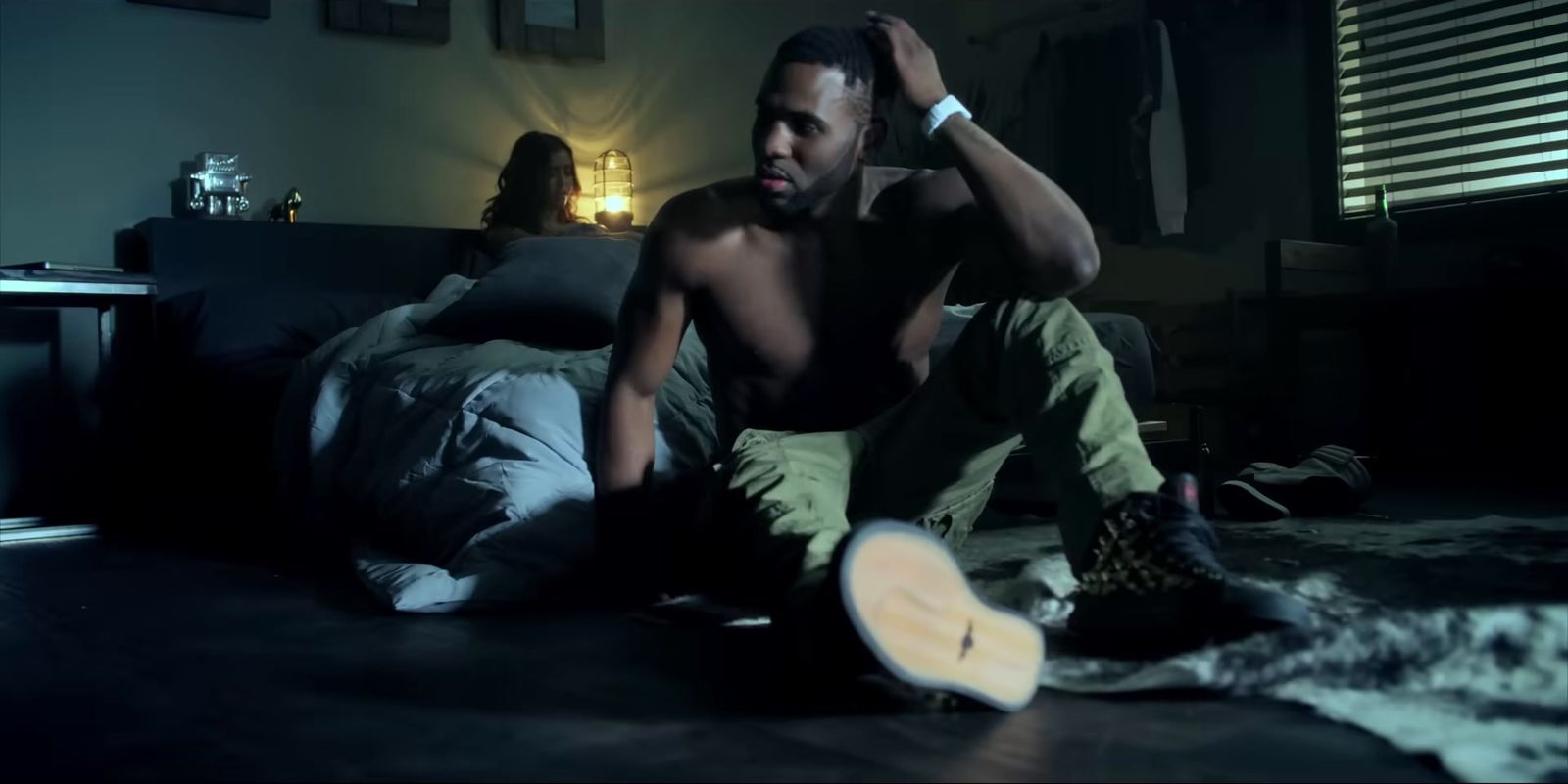 a shirtless man sitting on a bed in a dark room