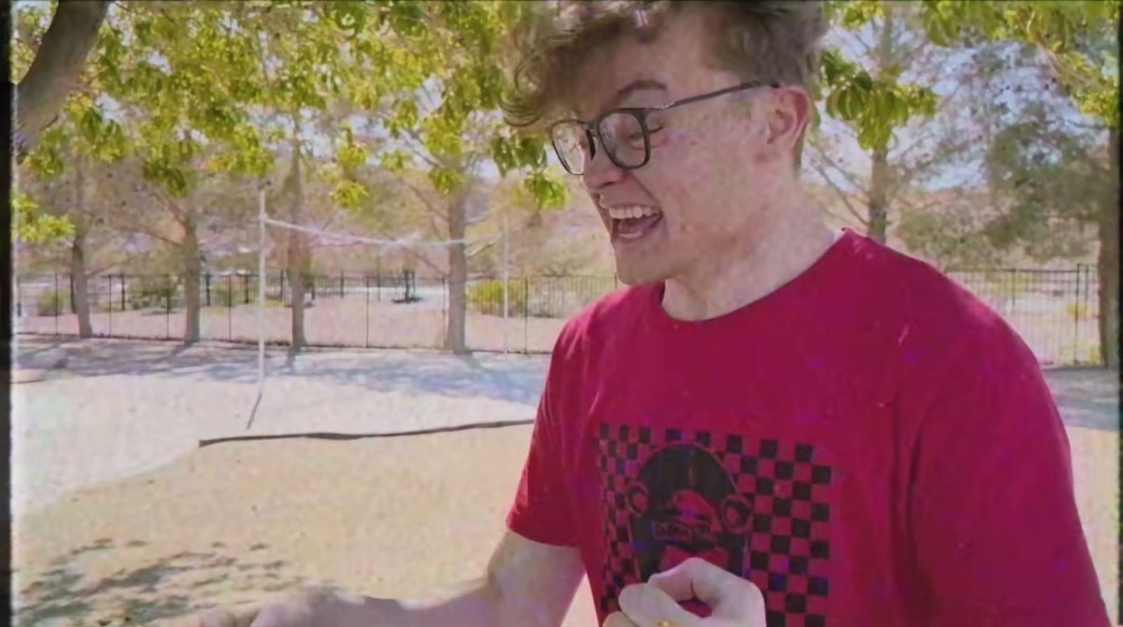 a man in a red shirt is holding a hot dog