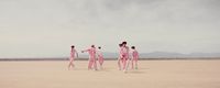 a group of people in pink suits walking across a desert