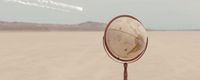 a mirror sitting on top of a metal pole in the middle of a desert