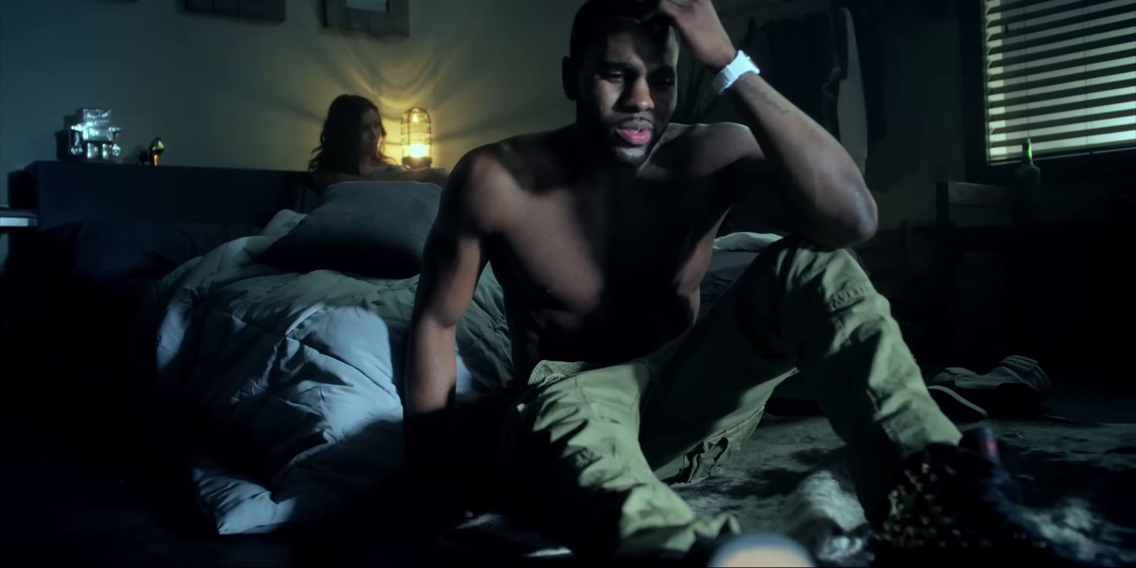 a shirtless man sitting on a bed in a dark room