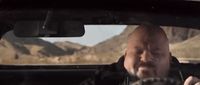 a man driving a car with mountains in the background