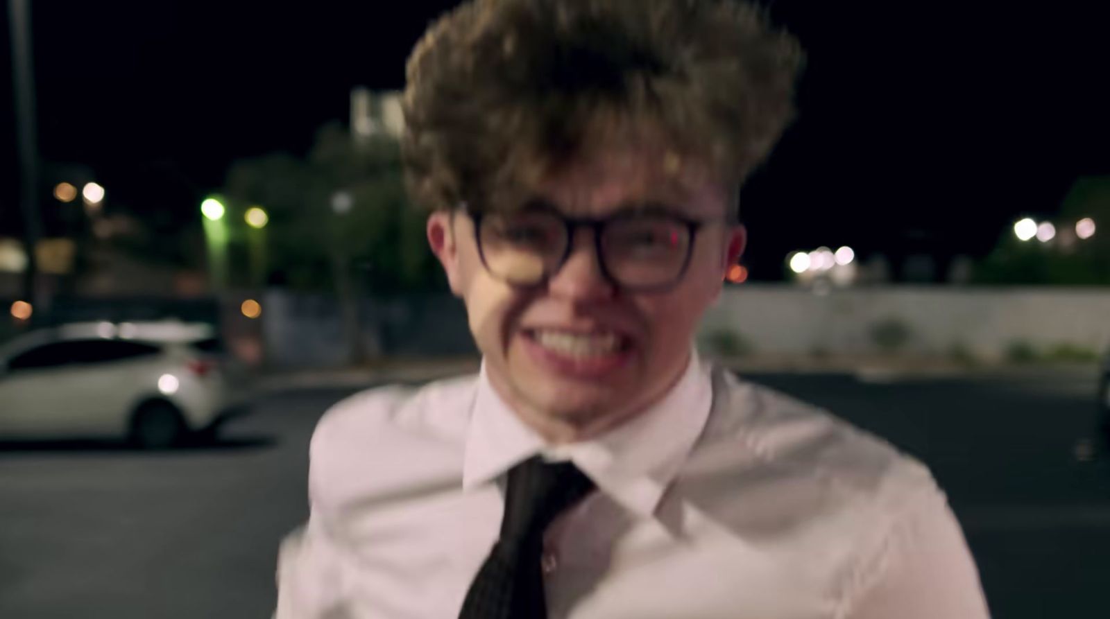 a man wearing glasses and a tie standing in a parking lot