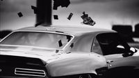 a black and white photo of a car with a bunch of money flying out of