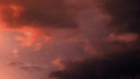 a plane flying through a cloudy sky at sunset