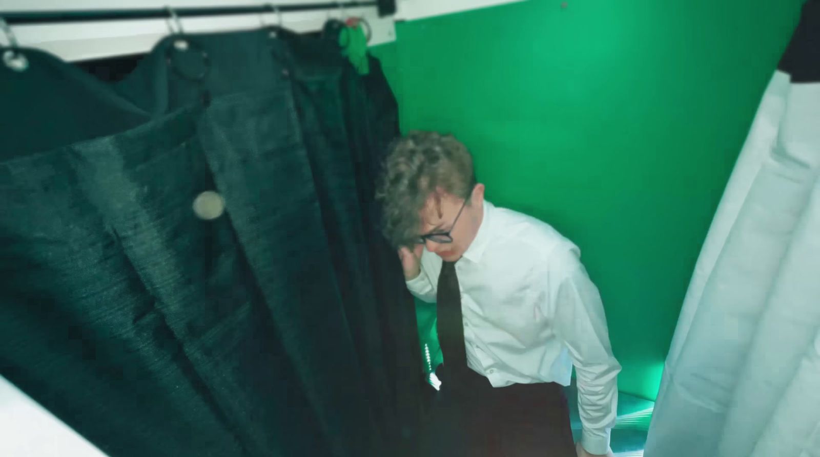 a man in a white shirt and tie standing in front of a curtain