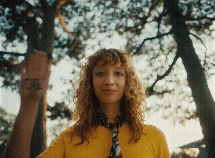 a woman with curly hair wearing a yellow shirt and tie